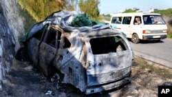 Sebuah minibus bergerak melewati mobil yang terbakar yang digunakan oleh komandan senior Hizbullah, Wissam Tawil, yang tewas dalam serangan Israel di desa Kherbet Selem, Lebanon selatan, pada 9 Januari 2024. (Foto: AP/Hussein Malla)