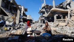 Perempuan Palestina sedang memanggang roti di depan sejumlah bangunan yang luluh lantak akibat serangan Israel, di Khan Younis di selatan Jalur Gaza, 30 November 2023. (Foto: REUTERS/Mohammed Salem)