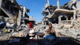 Perempuan Palestina sedang memanggang roti di depan sejumlah bangunan yang luluh lantak akibat serangan Israel, di Khan Younis di selatan Jalur Gaza, 30 November 2023. (Foto: REUTERS/Mohammed Salem)