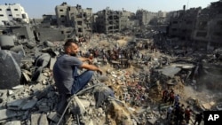 A man sits on the rubble as others wander among debris of buildings targeted by Israeli airstrikes in Jabaliya refugee camp, northern Gaza Strip, Nov. 1, 2023. 
