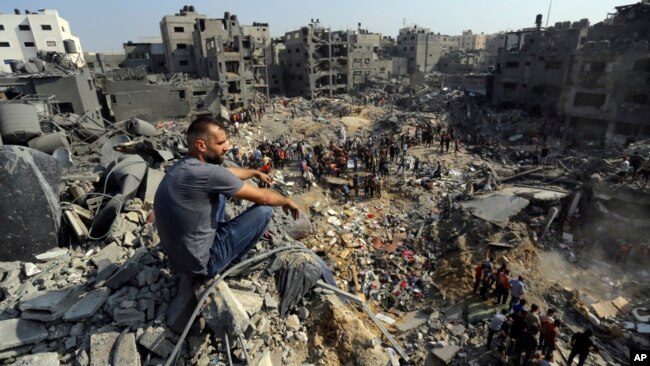 A man sits on the rubble as others wander among debris of buildings targeted by Israeli airstrikes in Jabaliya refugee camp, northern Gaza Strip, Nov. 1, 2023.