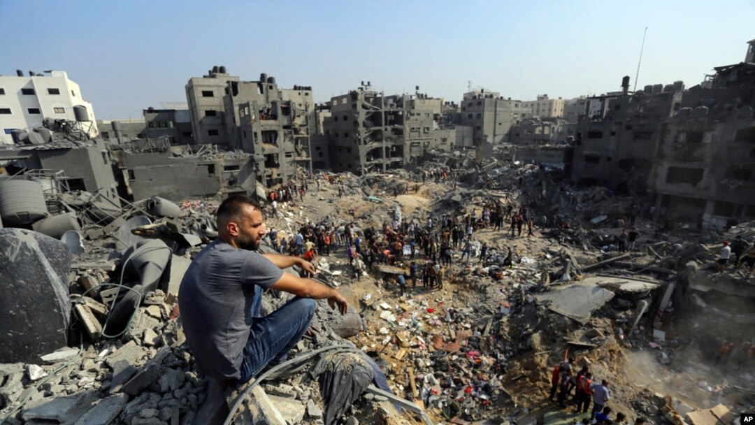 Seorang pria duduk di atas puing-puing, sedangkan orang-orang menyisir puing-puing yang menjadi target serangan udara Israel di kamp pengungsi Jabaliya di utara Jalur Gaza, 1 November 2023. (Foto: Abed Khaled/AP Photo)
