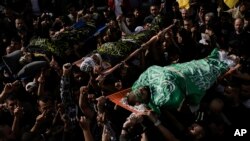 Mourners carry the bodies of three Palestinians draped in the Hamas and Islamic Jihad militant group flags during their funeral in the Jenin refugee camp, West Bank, Nov. 17, 2023.
