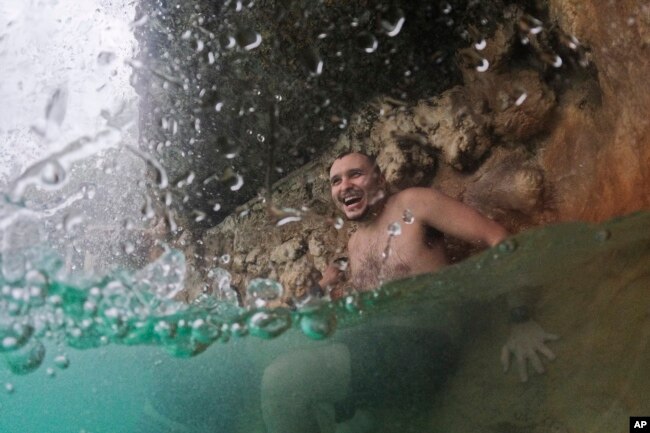 Un joven se refresca bajo una cascada en un día nublado con temperaturas en los 80 grados F (27 C) y tormentas de lluvia intermitentes, durante un respiro de una ola de calor en curso, en el Venetian Pool alimentado por acuífero en Coral Gables, Florida, el 27 de julio de 2023.