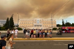 Asap dari kebakaran hutan terlihat di atas gedung parlemen Yunani di pusat kota Athena, Minggu, 11 Agustus 2024, setelah kebakaran di timur laut ibu kota memaksa evakuasi di daerah tersebut. (Derek Gatopoulos/AP)