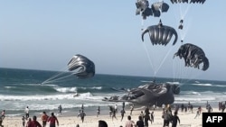 This image grab from an AFPTV video shows Palestinians running toward parachutes attached to food parcels, air-dropped from US aircrafts on a beach in the Gaza Strip on March 2, 2024.