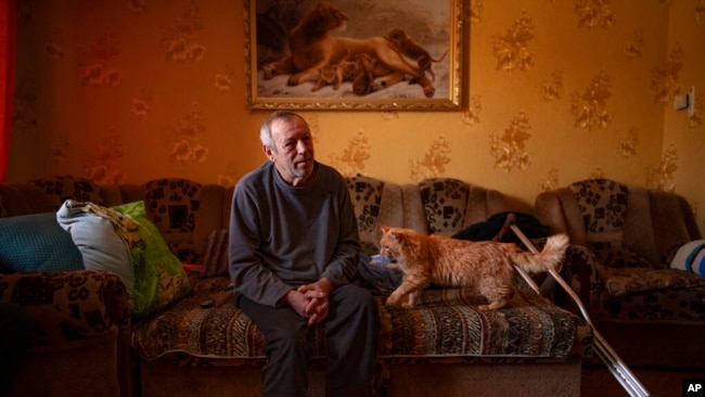 Oleksandr Rabenko, víctima de una mina terrestre, de 66 años, habla durante una entrevista mientras su gato Murzik se acerca, el domingo 19 de febrero de 2023. (Foto AP/Vadim Ghirda)