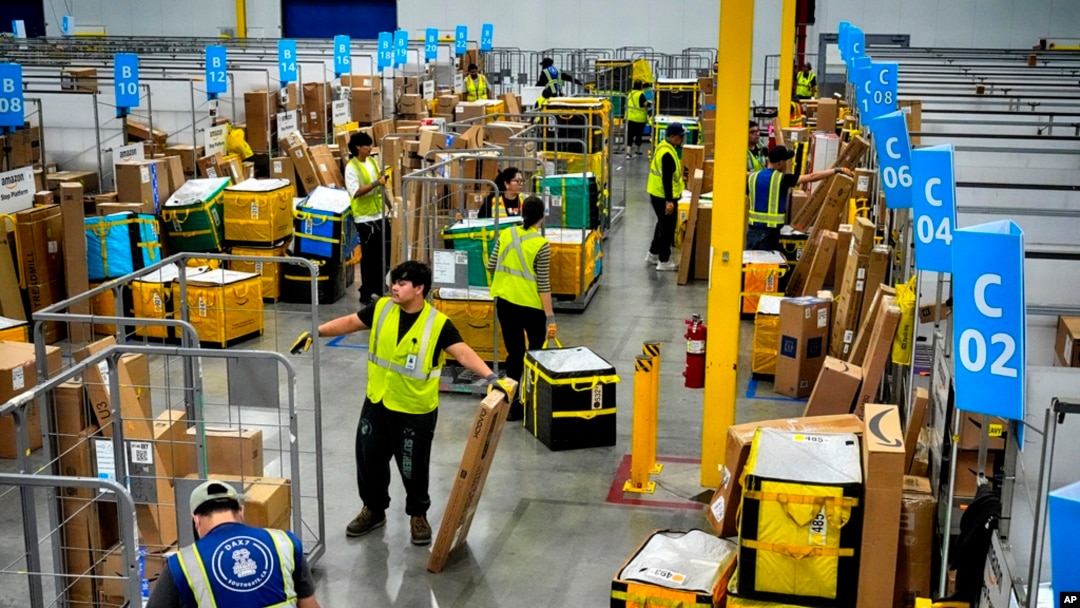 FILE - Employees load packages on carts at an Amazon delivery station, July 16, 2024, in South Gate, California.