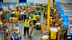 FILE - Employees load packages on carts at an Amazon delivery station, July 16, 2024, in South Gate, California.