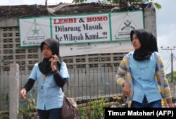 Dua perempuan Muslim berjalan melewati spanduk bertuliskan 'homoseksual dan lesbian dilarang memasuki lingkungan kami' di Bandung, Jawa Barat. (Foto: AFP/Timur Matahari)