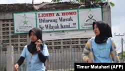 FILE - Dua perempuan Muslim berjalan melewati spanduk bertuliskan 'homoseksual dan lesbian dilarang memasuki lingkungan kami' di Bandung, Jawa Barat. (Foto: AFP/Timur Matahari)