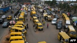 Commuters walk next to parked public transport mini buses at Ojodu Berger bus station in Lagos, on June 1, 2023. Nigerians are lamenting the effect removal of the fuel subsidy is having on the economy, especially the massive hike in transport fare and cost of goods and services. 
