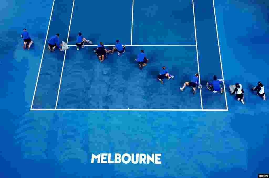 Ground workers dry out the court during the second round match of the Australian Open tennis championships between Poland&#39;s Iga Swiatek and Danielle Collins of the United Staes, as the match is interrupted by rain, in Melbourne, Australia.