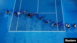 Ground staff members dry the court during the second round match of the Australian Open tennis championships between Poland&#39;s Iga Swiatek and Danielle Collins of the U.S. as the match is interrupted due to rain in Melbourne, Australia.