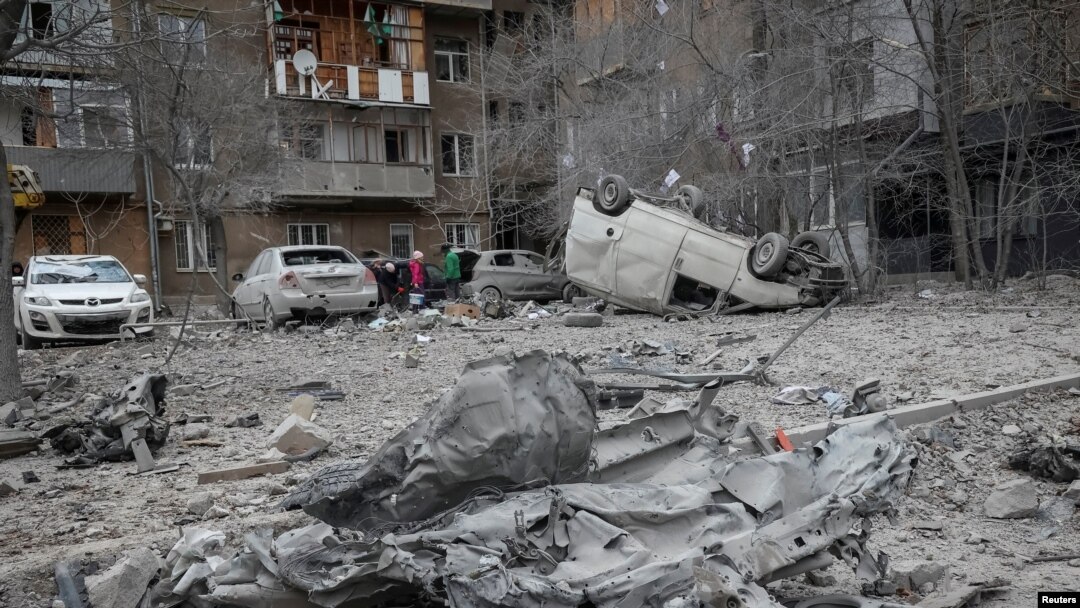 Warga setempat berdiri di dekat gedung apartemen dan mobil mereka yang rusak akibat serangan rudal Rusia di kota Kharkiv, Ukraina, 8 Desember 2023.