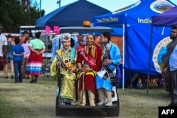 Perempuan mengenakan kostum adat, duduk di kereta emas saat pertemuan budaya di tempat pekan raya Comanche Nation di Lawton, Oklahoma, 30 September 2023. (CHANDAN KHANNA / AFP)