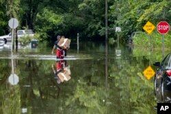 Savannah Fire Advanced Firefighters Andrew Stevenson, front, and Ron Strauss carry food to residents in the Tremont Park neighborhood that where stranded in flooding from Tropical Storm Debby, Aug. 6, 2024, in Savannah, Georgia.