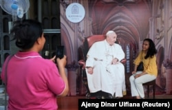 Seorang perempuan berpose dengan potongan gambar Paus Fransiskus di Katedral Jakarta menjelang kunjungannya, di Jakarta, 31 Agustus 2024. (Foto: REUTERS/Ajeng Dinar Ulfiana)