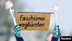 FILE - A protester displays toilet brushes and a sign reading, "Brush fascism away" at a demonstration against the Alternative for Germany (AfD) party, right-wing extremism and for the protection of democracy in Hamburg, Germany, Feb. 25, 2024. 