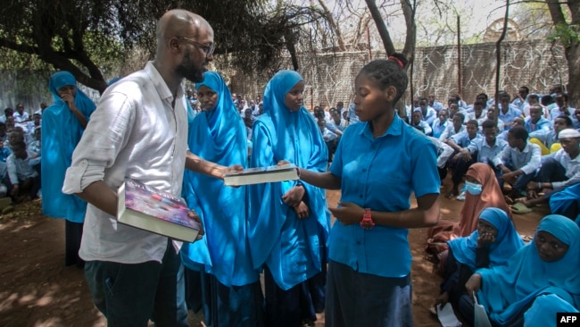 This handout picture taken on Oct. 25, 2023, shows Abdullahi Mire, left, winner of the U.N. refugee agency's prestigious Nansen Award distributing books to refugee students in Kenya's Dadaab refugee camp. (AFP Photo/UNHCR)
