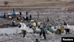 FILE - Porters cross a stream while lugging goods to Iran, at the border near Sulaymaniyah, Iraq, Feb. 15, 2012.