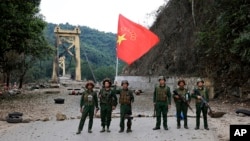 FILE - Anggota Tentara Aliansi Demokratik Nasional Myanmar berpose dengan bendera kelompok tersebut di depan jembatan Kunlong di negara bagian Shan, Myanmar, 12 November 2023. 