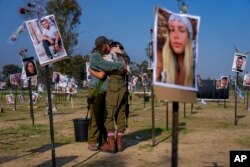Israeli soldiers embrace next to photos of people killed and taken captive by Hamas militants on Oct. 7, near kibbutz Re'im, on Dec. 1, 2023.