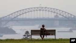 FILE - A man watches the sunset from a park bench in the Eastern suburbs of Sydney, Nov. 16, 2020. 