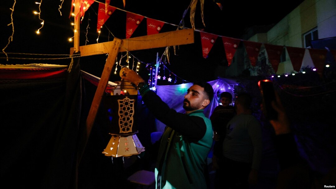 Seorang pria Palestina menggantungkan lentera di tenda pengungsian untuk menyambut datangnya Ramadan, di tengah konflik Israel-Hamas, di Rafah, di selatan Jalur Gaza, 9 Maret 2024. (Foto: REUTERS/Mohammed Salem)
