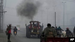 A tractor releases smoke as it moves along a road as smog envelops the area, in Lahore, Pakistan, Jan. 15, 2024.