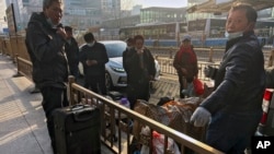 FILE - Migrant workers with their luggage take a break outside the West Railway Station before catching their trains in Beijing, Jan. 6, 2023.