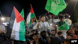 Palestinian prisoners (wearing gray jumpers) released from the Israeli Ofer military facility, in exchange for hostages freed by Hamas in Gaza, wave flags and chant slogans as they are paraded in Baytunia in the occupied West Bank, Nov. 24, 2023.