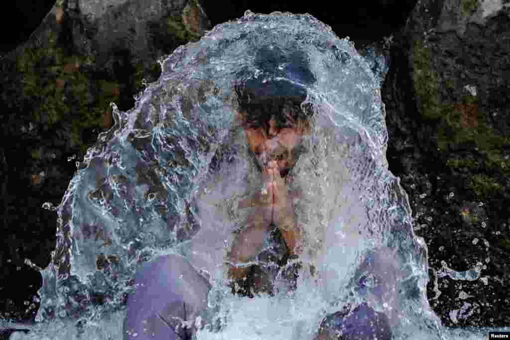 A man reacts as he cools off under a water pipe from a canal during hot and humid weather, in the outskirts of Peshawar, Pakistan.