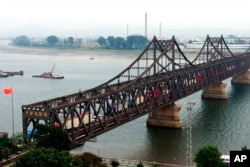 FILE - Trucks cross the bridge connecting Dandong, China, and Sinuiju, North Korea, Sept. 4, 2017. North Korea fears that planned Chinese telecom facilities, including some near Dandong, could cause "serious interference."