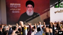FILE — Supporters of the Iranian-backed Hezbollah group raise their fists and cheer as Hezbollah leader Sayyed Hassan Nasrallah appears via a video link during a rally in Beirut, Lebanon, Nov. 3, 2023. 