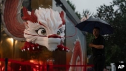 A security guard stands in the rain next to a dragon depiction in a shopping district in Beijing, July 30, 2024.