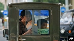 A woman cools herself with a fan as she rides a tricycle with a child on a hot day in Beijing, July 3, 2023.