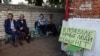 FILE - Russian residents sit near a shelter where they hid while Ukrainian and Russian forces fought in Sudzha, which is controlled by Ukrainian army, Kursk region, Russia, Aug. 16, 2024. The sign says: "There are peaceful people in the basement, there are no soldiers."