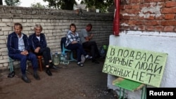 FILE - Russian residents sit near a shelter where they hid while Ukrainian and Russian forces fought in Sudzha, which is controlled by Ukrainian army, Kursk region, Russia, Aug. 16, 2024. The sign says: "There are peaceful people in the basement, there are no soldiers."