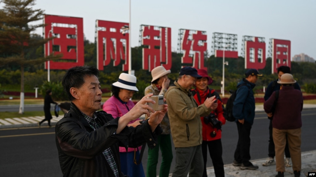 中国福建厦门竖立起一个台湾金门岛可以看到的“一国两制统一中国”的大型标语牌，旅游者在前拍照。（2024年1月12日）