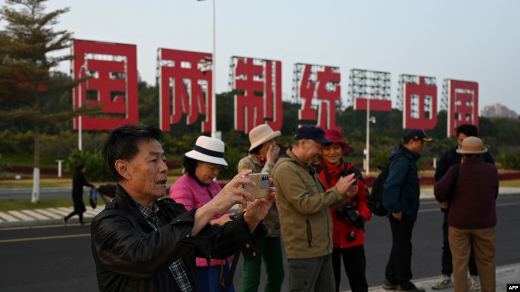 中国福建厦门竖立起一个台湾金门岛可以看到的“一国两制统一中国”的大型标语牌，游客在前拍照。（2024年1月12日）