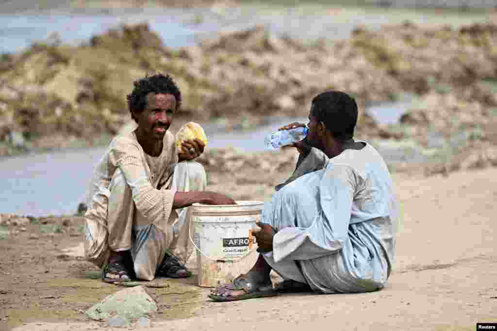 A man drinks water while another holds a loaf of bread, following devastating floods, in Port Sudan, Sudan.