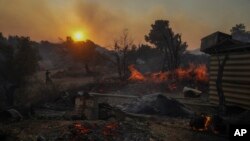 A man on a motorcycle looks on as a shipyard which is on fire in Mandra west of Athens, on Tuesday, July 18, 2023. In Greece, where a second heatwave is expected to hit Thursday, three large wildfires burned outside Athens for a second day. 