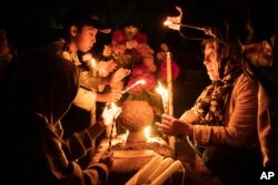 People hold candles over a tomb decorated with flowers at a cemetery in Atzompa, Mexico, late on Oct. 31, 2023.