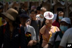 A woman uses a fan to shield herself from the sun as she walks among crowds for a Dragon Boat festival event at a public park on an unseasonably hot day in Beijing, Thursday, June 22, 2023.