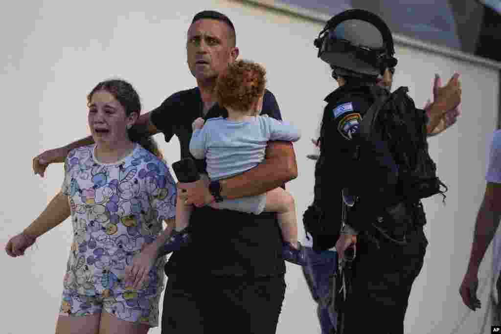 Israeli police officers evacuate a family from a site hit by a rocket fired from the Gaza Strip, in Ashkelon, Oct. 7, 2023. The rockets were fired as Hamas announced a new operation against Israel.