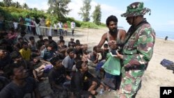 An Indonesian soldier inspects the identification of ethnic Rohingya men after they land on a beach in Pidie, Aceh province, Indonesia, Dec. 10, 2023. 