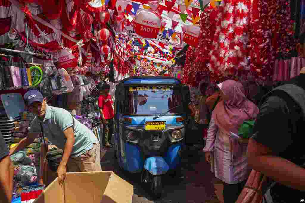 A three-wheeled motorized vehicle drives past people in an alley where vendors have displayed national flags and decoration material for sale ahead of country's Independence anniversary in Jakarta, Indonesia.