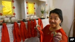 Mee Vang Yang holds her father's shaman bells in front of the altar in her living room in St. Paul, Minnesota, Nov. 17, 2023. Vang Yang carried them across the Mekong River as the family fled the Communist takeover of her native Laos four decades ago. 