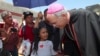 El Paso Catholic Bishop Mark Seitz talks with Celsia Palma, 9, of Honduras, as they walk to the Paso Del Norte International Port of Entry, June, 27, 2019, in Juarez, Mexico.